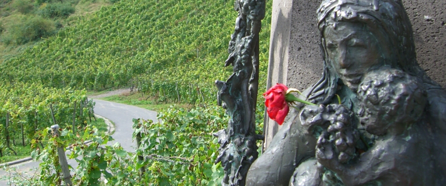 Das Bild zeigt ein Teilstück eines Kunstwerks in einem Weinberg, zu sehen ist eine Frau mit einem Kind, das Trauben in der Hand hält, den Figuren ist - nicht vom Fotografen - eine Rose zugesteckt worden; in Zukunft wäre die Nutzung dieses Bild vermutlich bereits vergütungspflichtig